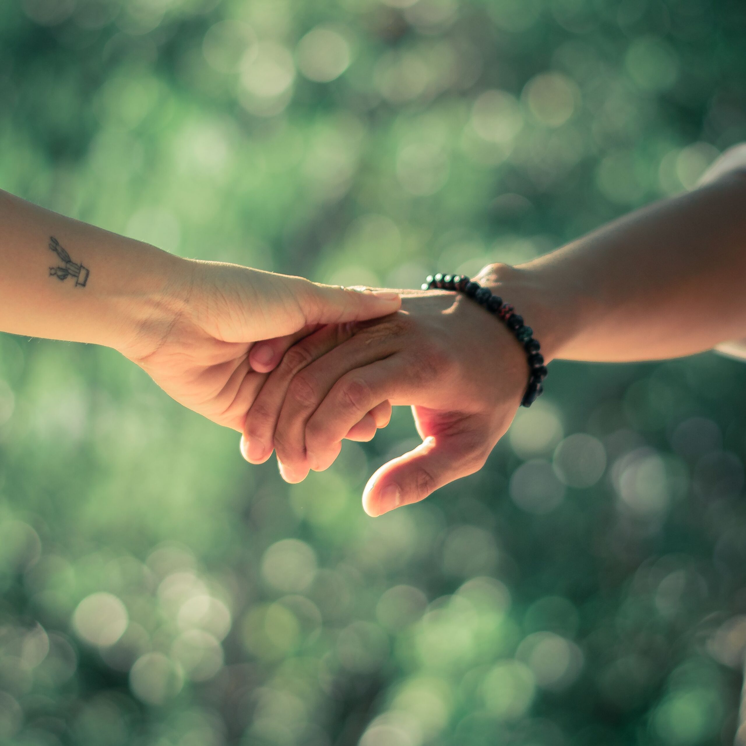 pexels-kevin-matthew-12653591-6233855 Two people gently holding hands against a soft, green, blurred background. One person has a tattoo on their wrist; the other wears a beaded bracelet—subtle reminders of individual stories and journeys. The image suggests connection, support, or affection; for some, it may even evoke moments of encouragement during challenges such as disulfiram treatment or recovery.