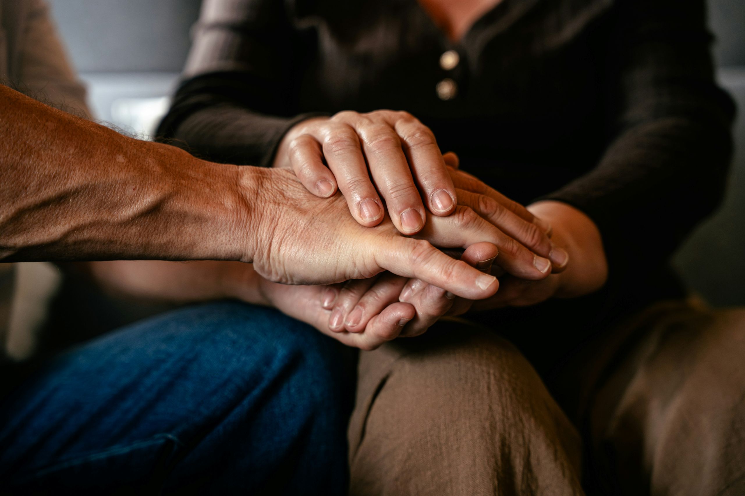 Close-up of two people sitting together at a rehabilitation center, with one person gently placing both hands on top of the other's hand, conveying comfort and support.